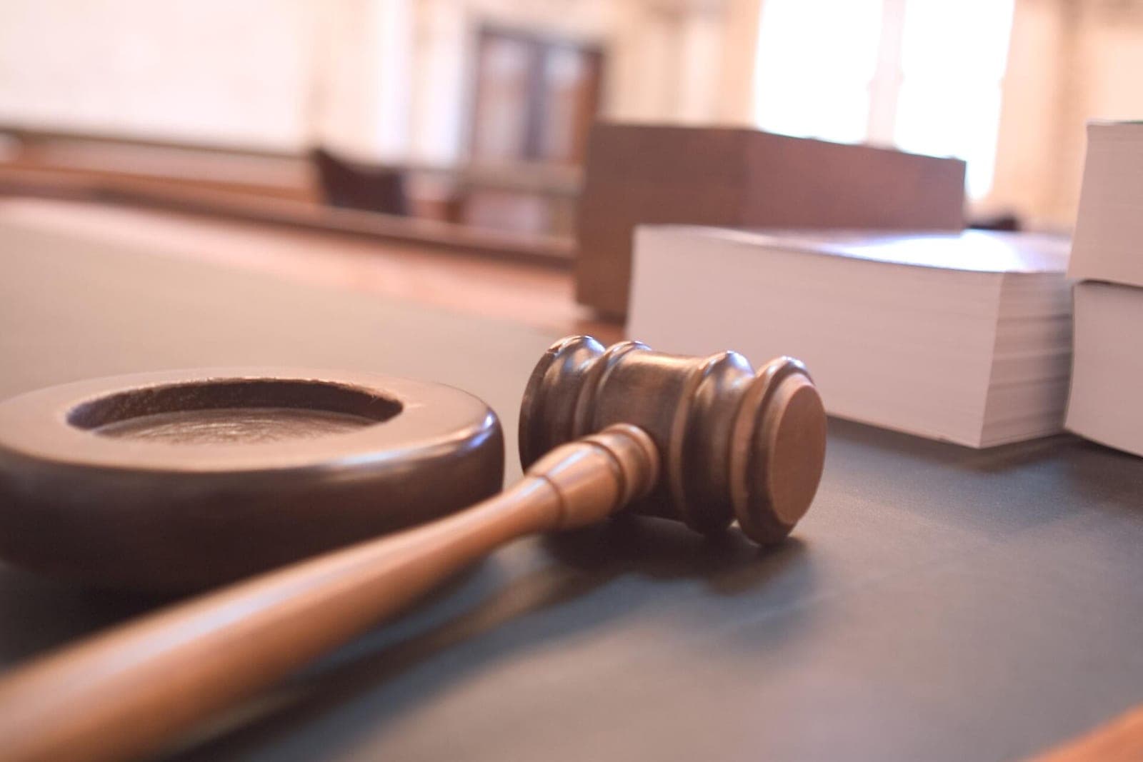 A wooden gavel and its sound block on a courtroom bench beside thick stacks of paper
