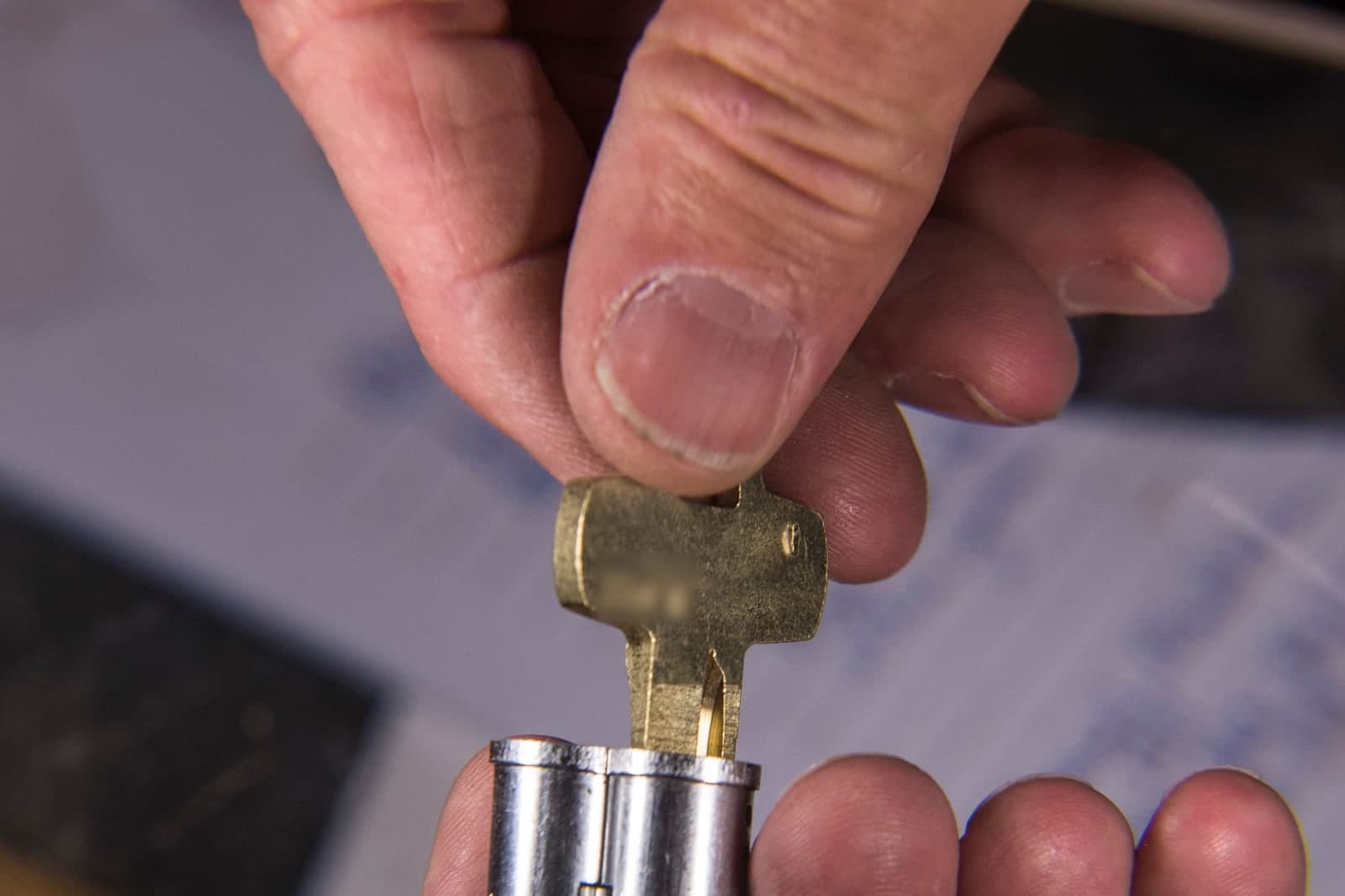 A locksmith's hands fit a brass key into a lock cylinder in a workshop