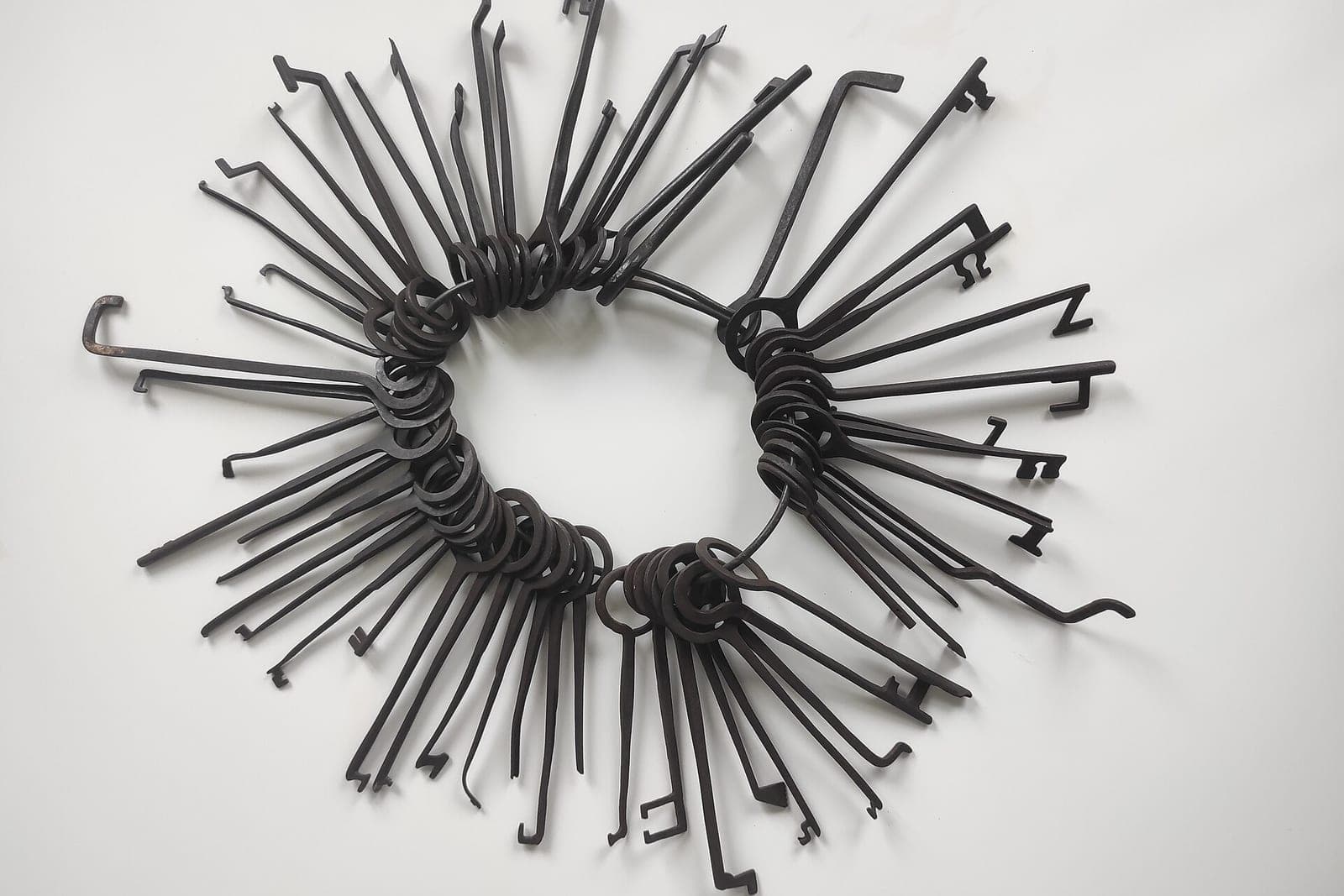 A large ring of dark metal keys and picks laid out in a circle on a white surface