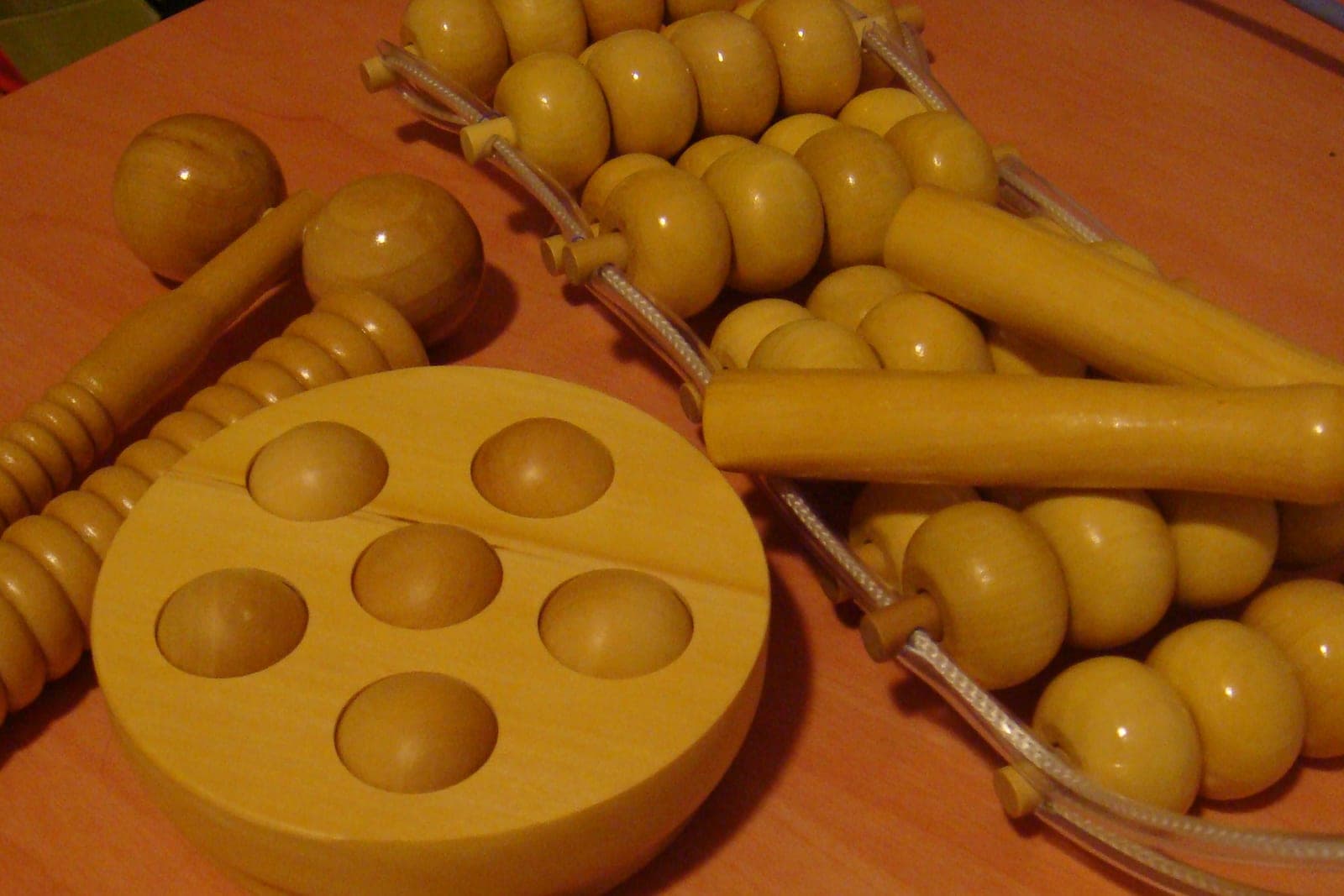 Wooden massage rollers, a round tray of wooden balls and a beaded back roller on a table