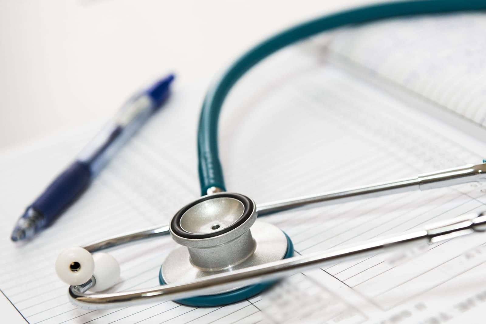 A stethoscope and a blue pen rest on a printed sheet ruled into rows