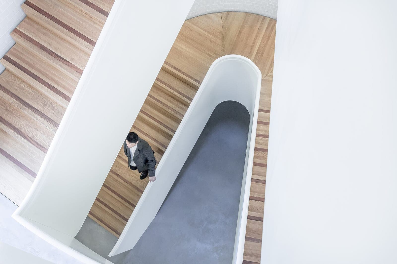 A person walks down a curved wooden staircase seen from above