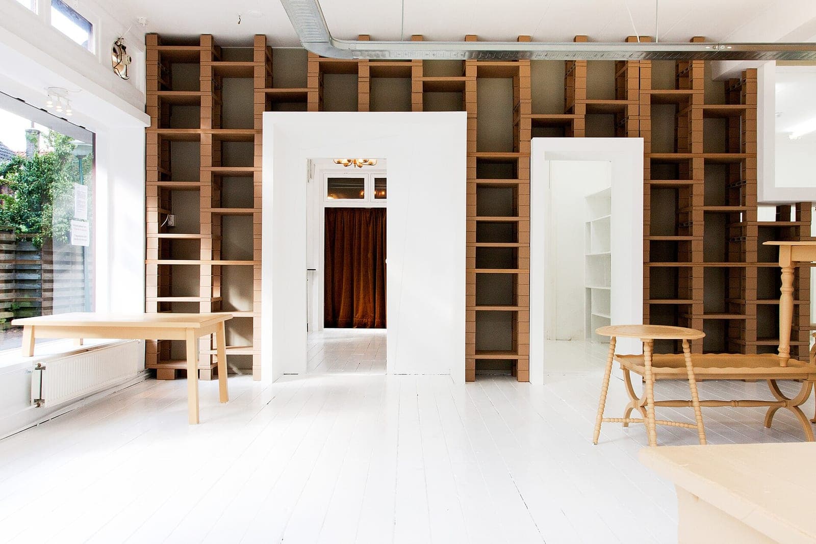 A bright, mostly empty room with white floors, open doorways and tall wooden shelving along the back wall