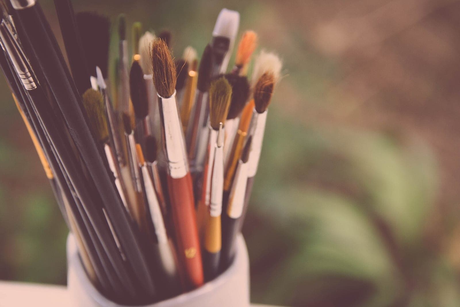 Paintbrushes of many sizes standing in a white cup