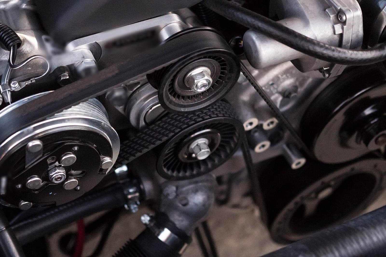 Close view of an engine's drive belt wrapped around metal pulleys