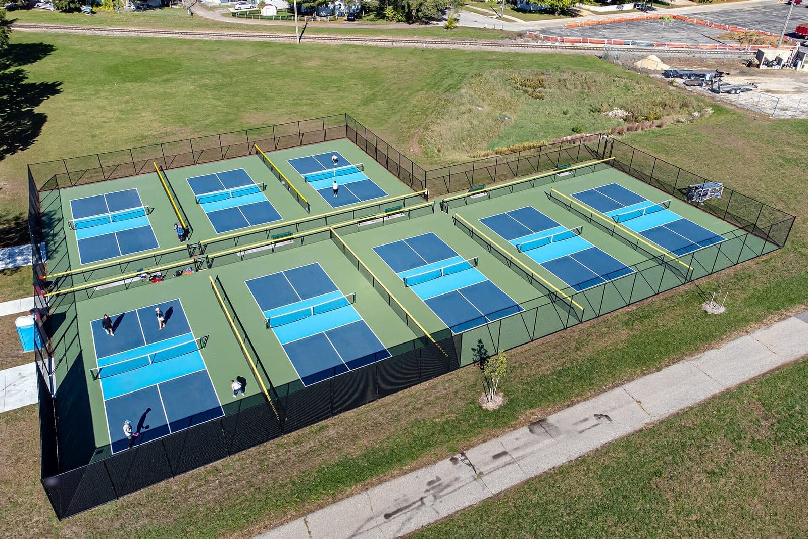 Overhead view of several fenced pickleball courts with a few adults playing on a sunny day