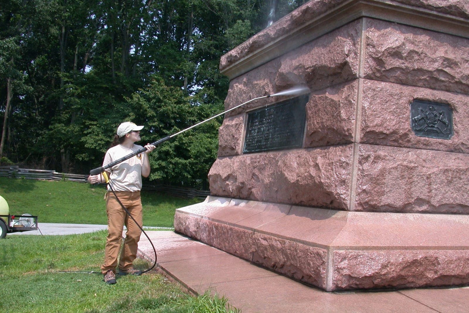 A worker pressure washes the red granite base of a monument on a sunny day