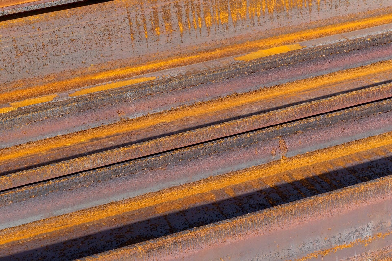 Rows of rusty steel I-beams stacked side by side in bright sunlight
