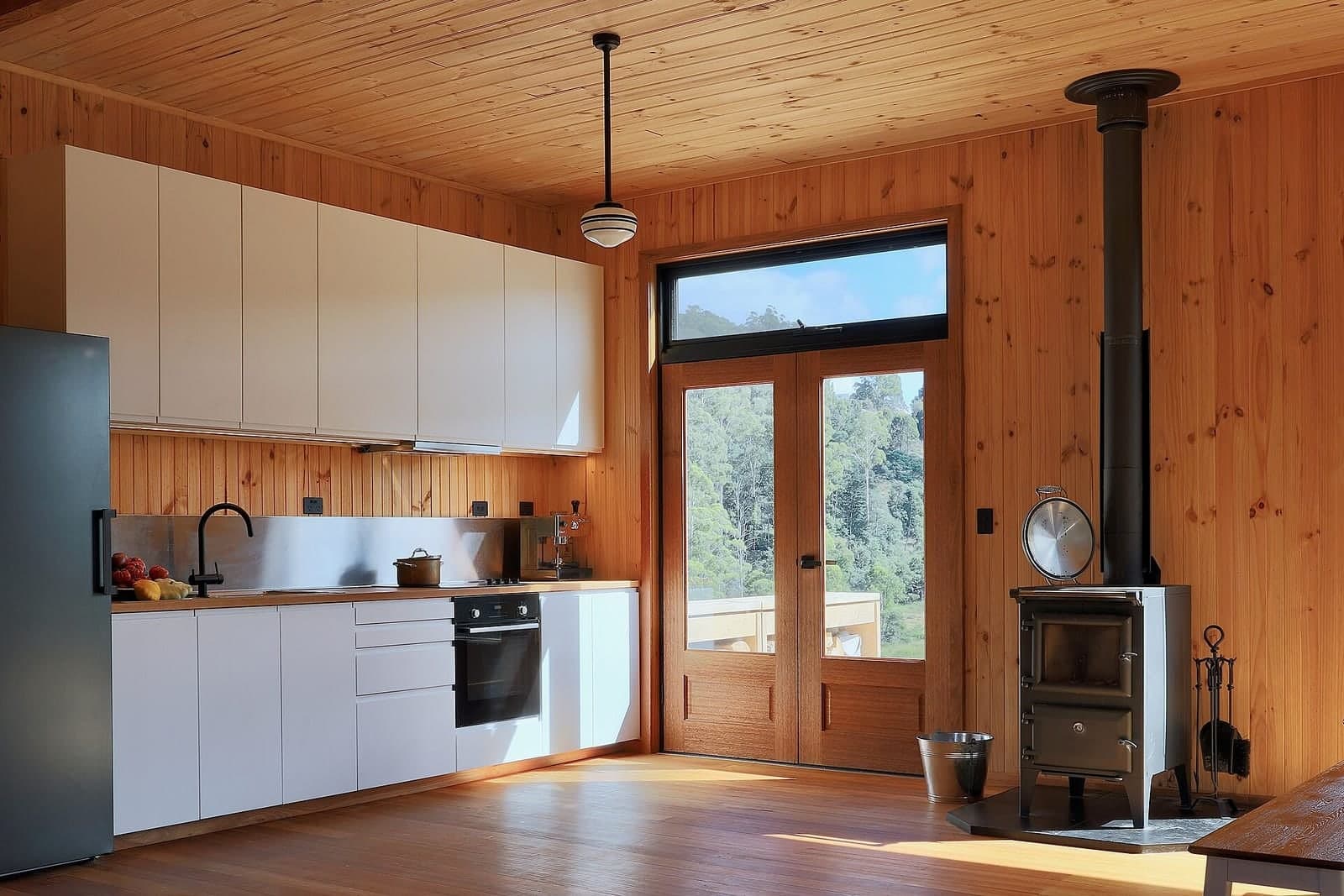 A wood-lined kitchen with white cabinets, glass doors and a small wood stove