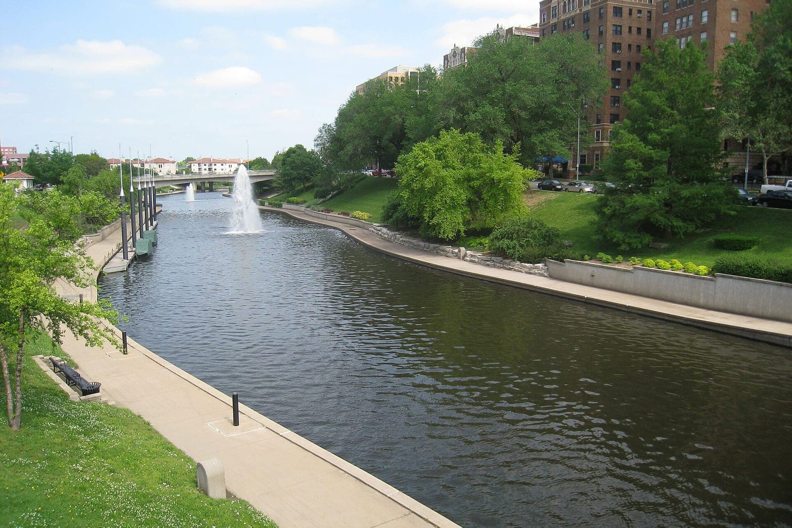 A tree-lined creek walk with a fountain beside tall brick buildings at the Country Club Plaza in Kansas City