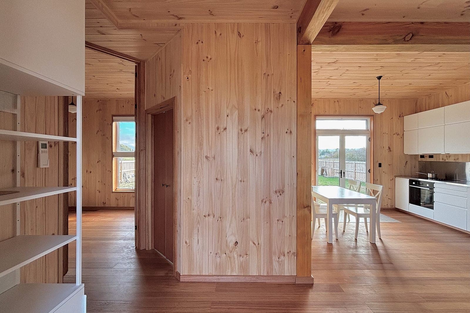 A wood-lined house with a white dining table, a white kitchen and glass doors to the yard