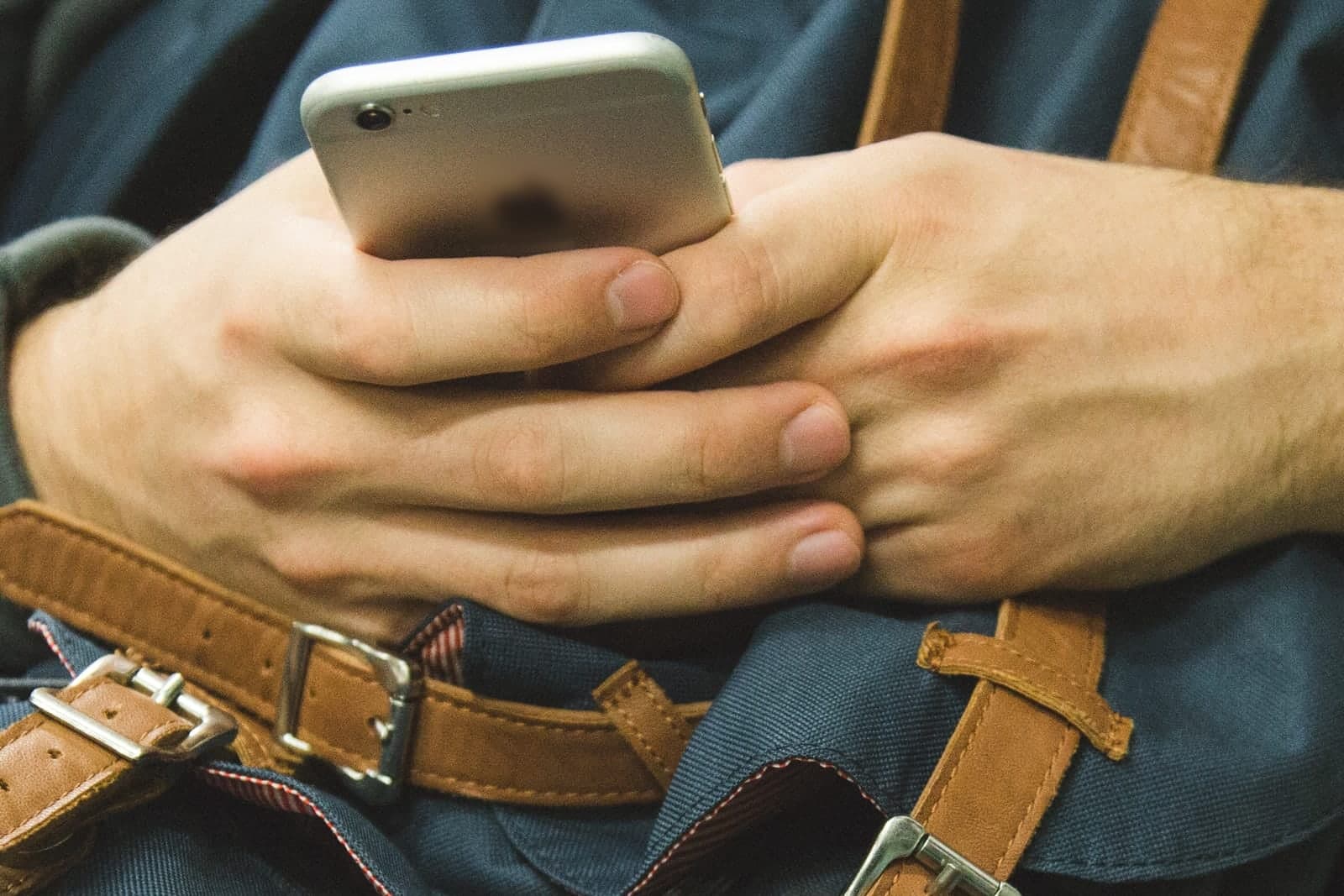 Hands hold a phone above a blue backpack with brown leather straps