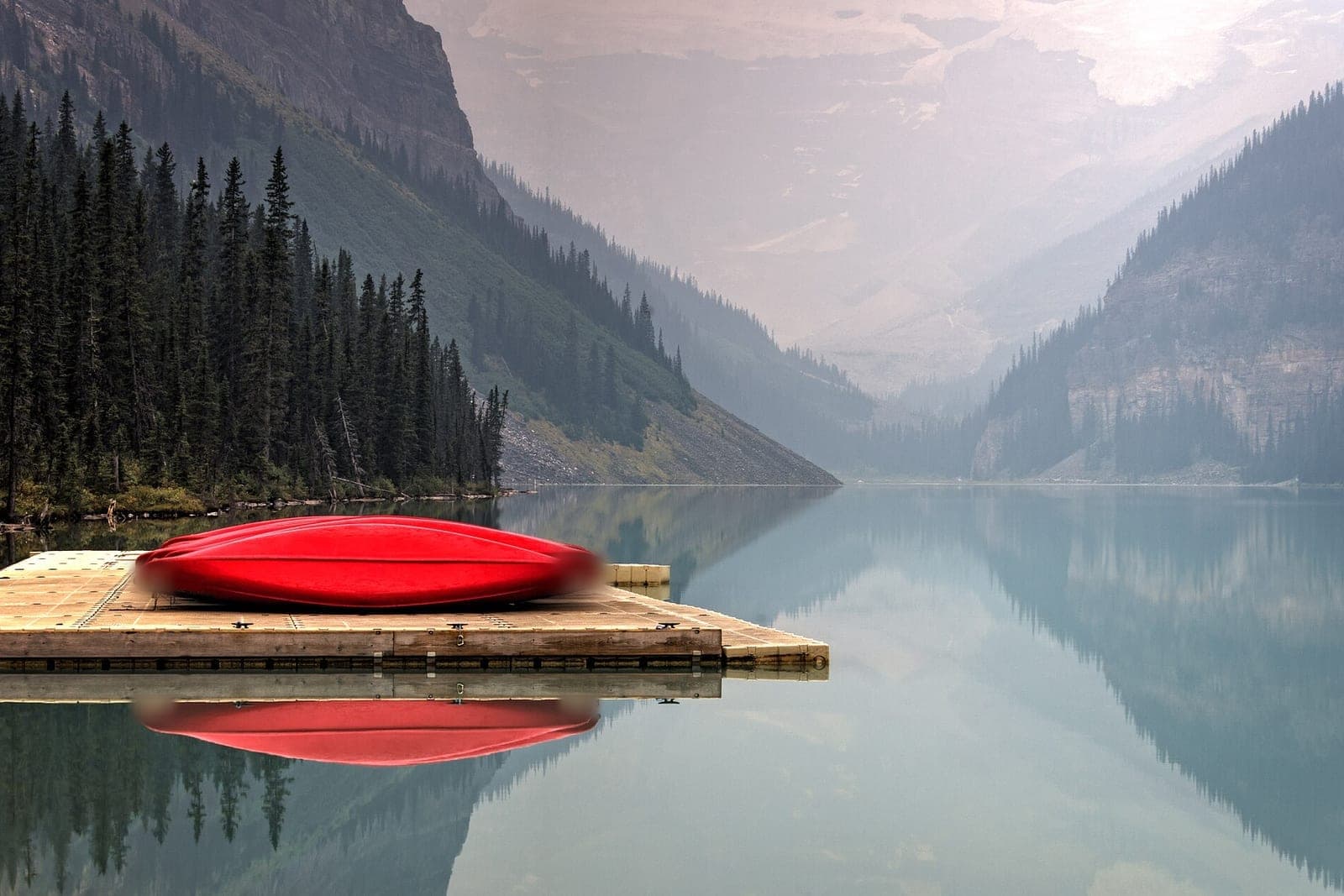 Red canoes stacked upside down on a floating dock beside a still lake and pine forest