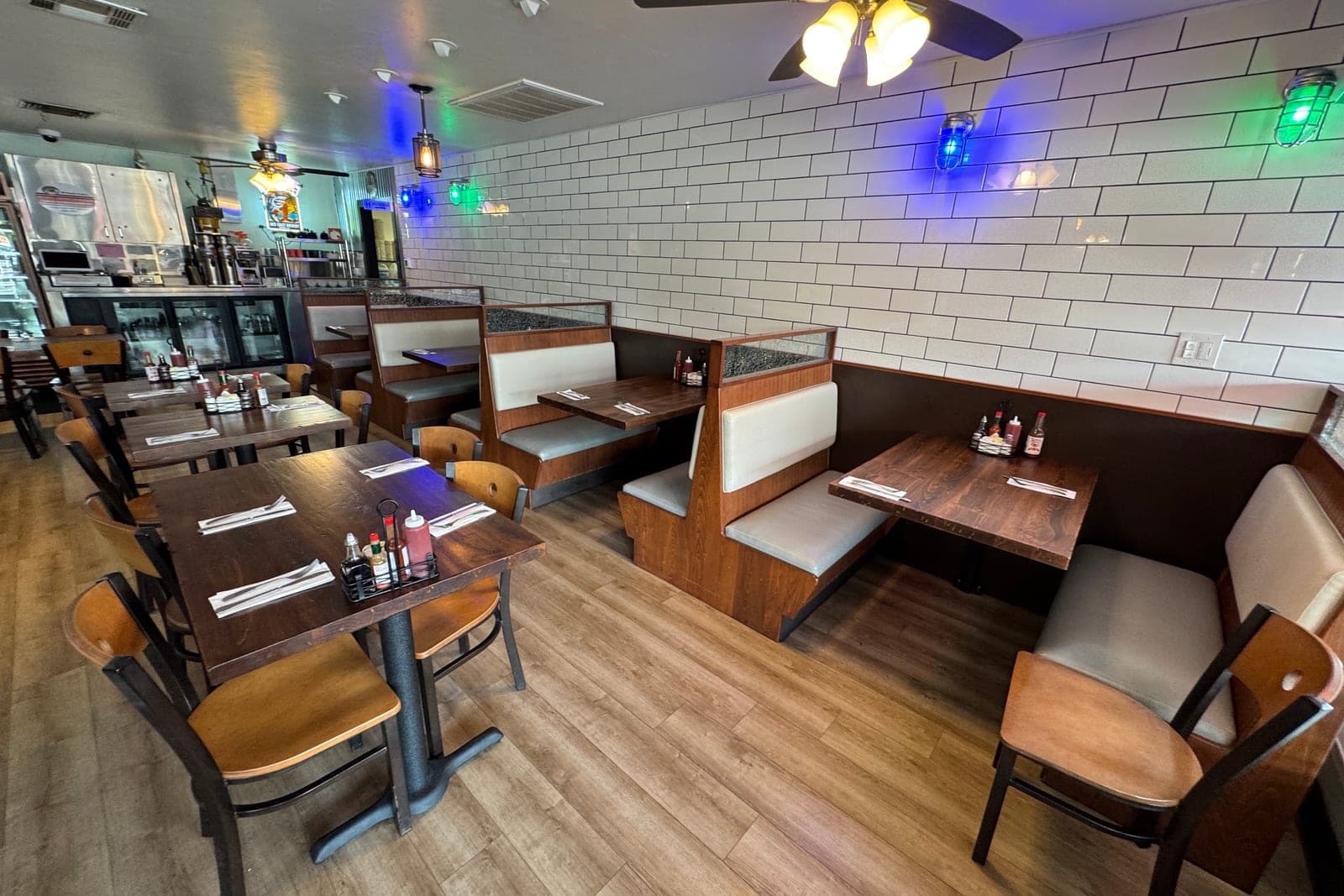 An empty restaurant dining room with booths and wooden tables set with rolled silverware and condiment caddies