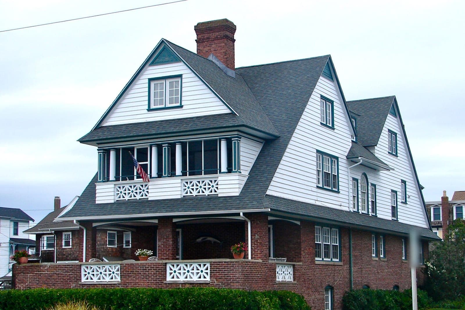 A white clapboard house with a gray asphalt shingle roof, steep gables and a brick chimney
