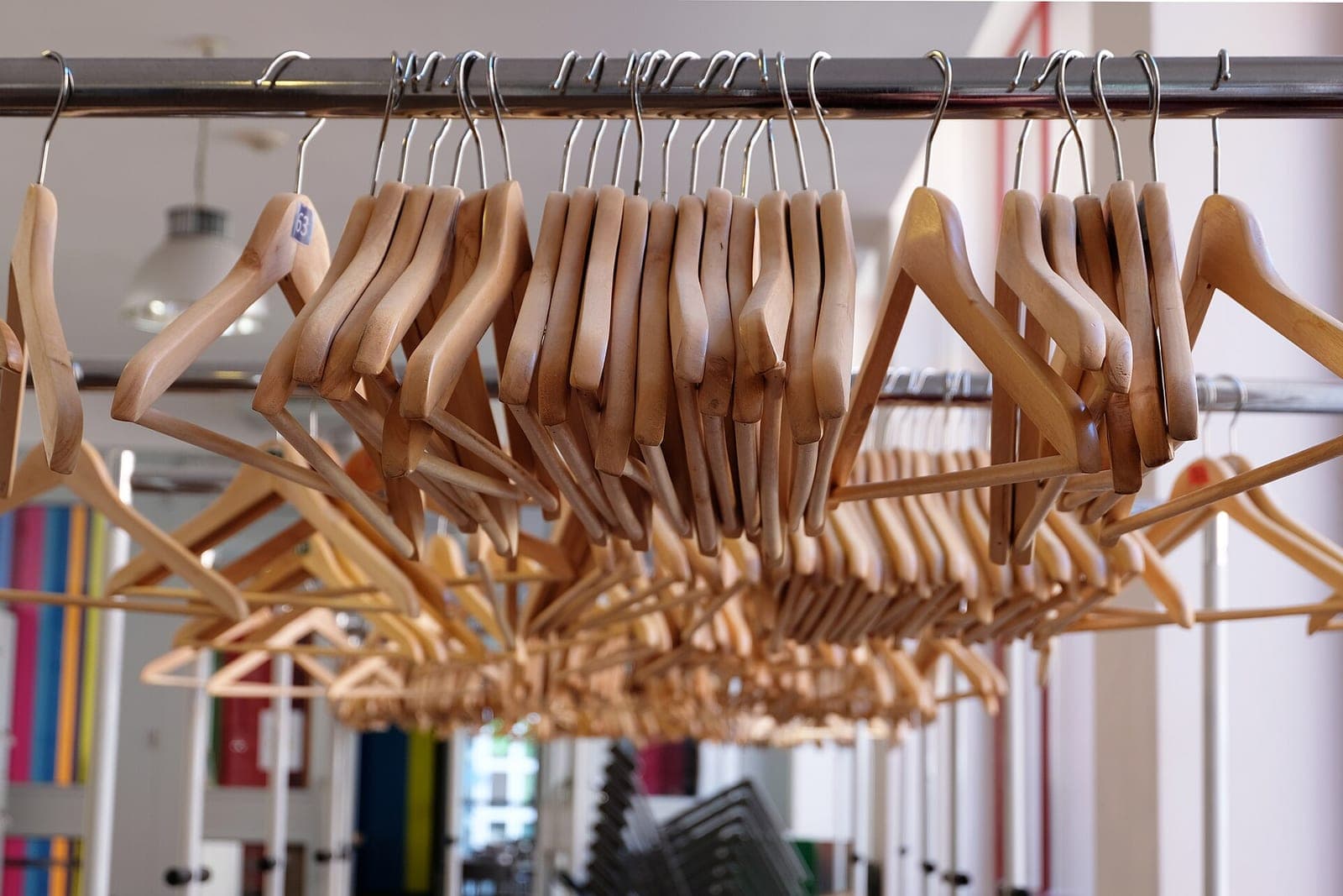 Rows of empty wooden clothes hangers hang from a metal rail in a bright room