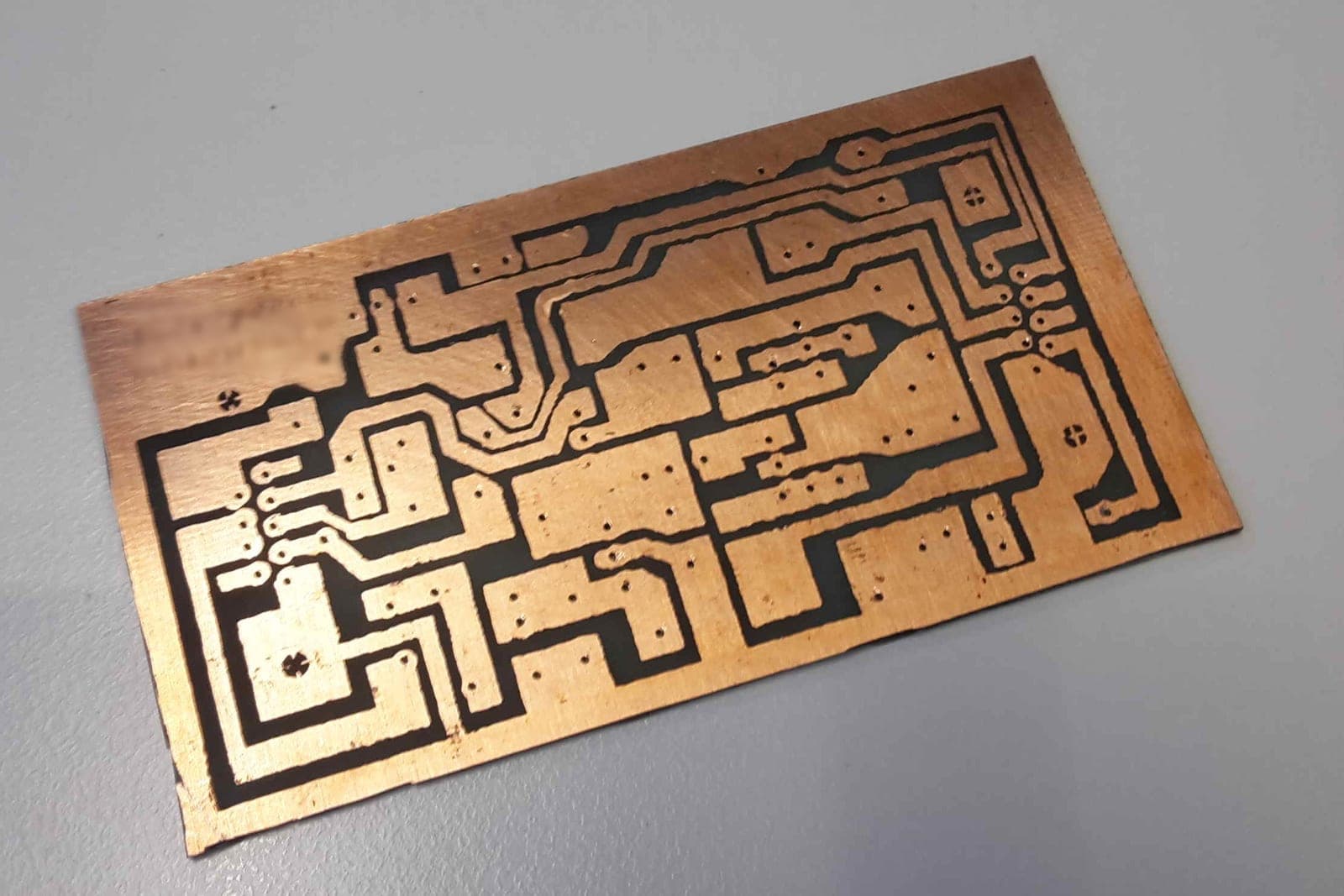 A small etched copper circuit board lies on a plain gray table