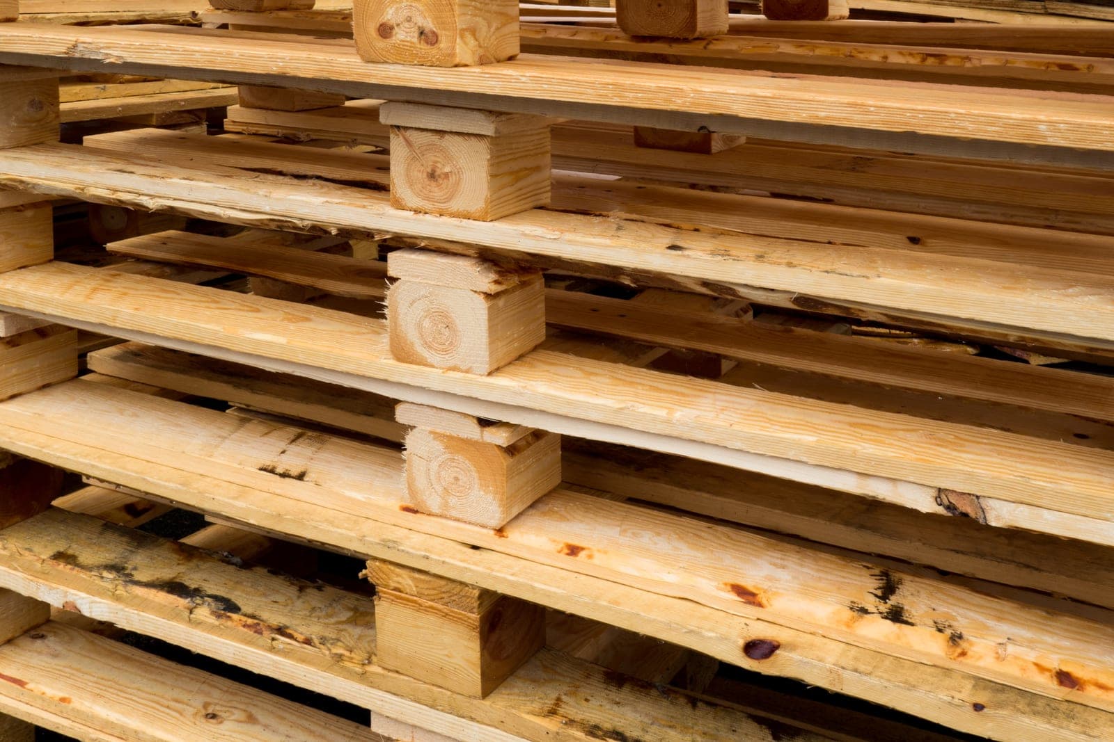 Empty wooden pallets stacked in a tall pile with their pale boards and blocks showing