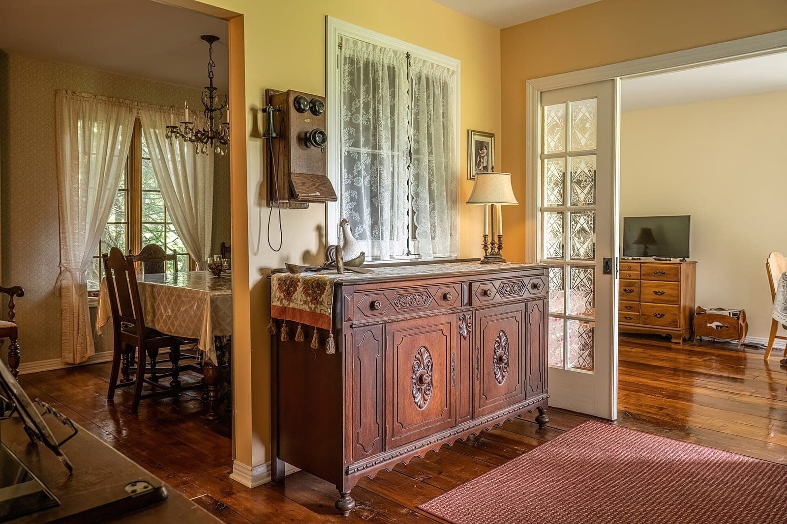A carved wooden sideboard stands between a dining room and a sitting room with wide plank floors
