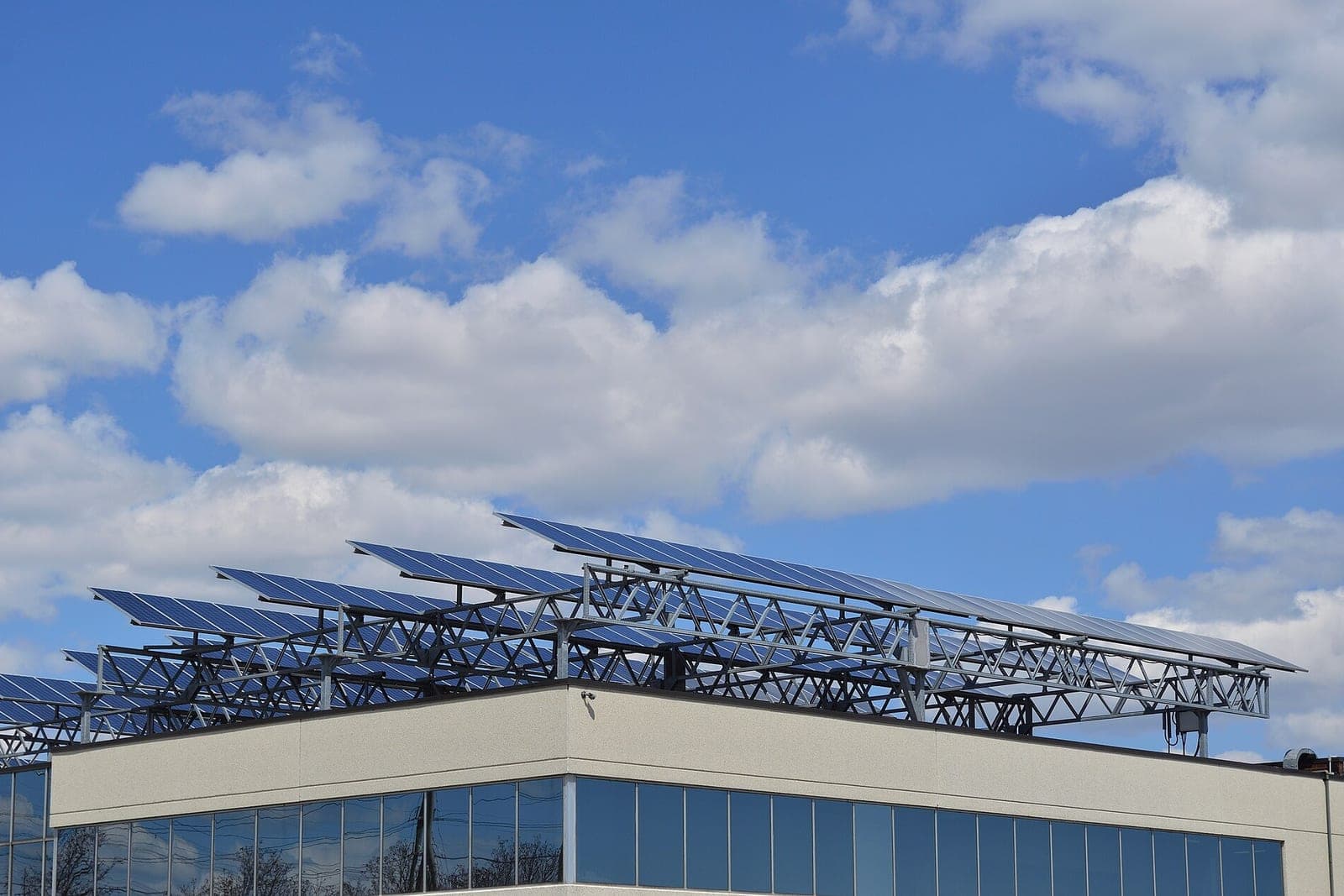 Solar panels on steel frames along the roof of a low office building under a cloudy sky
