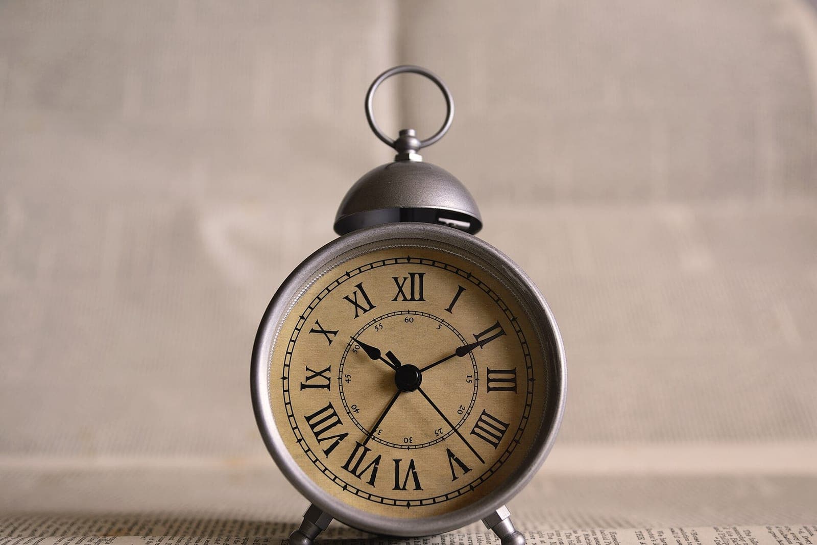 A small metal alarm clock with Roman numerals against a soft beige background