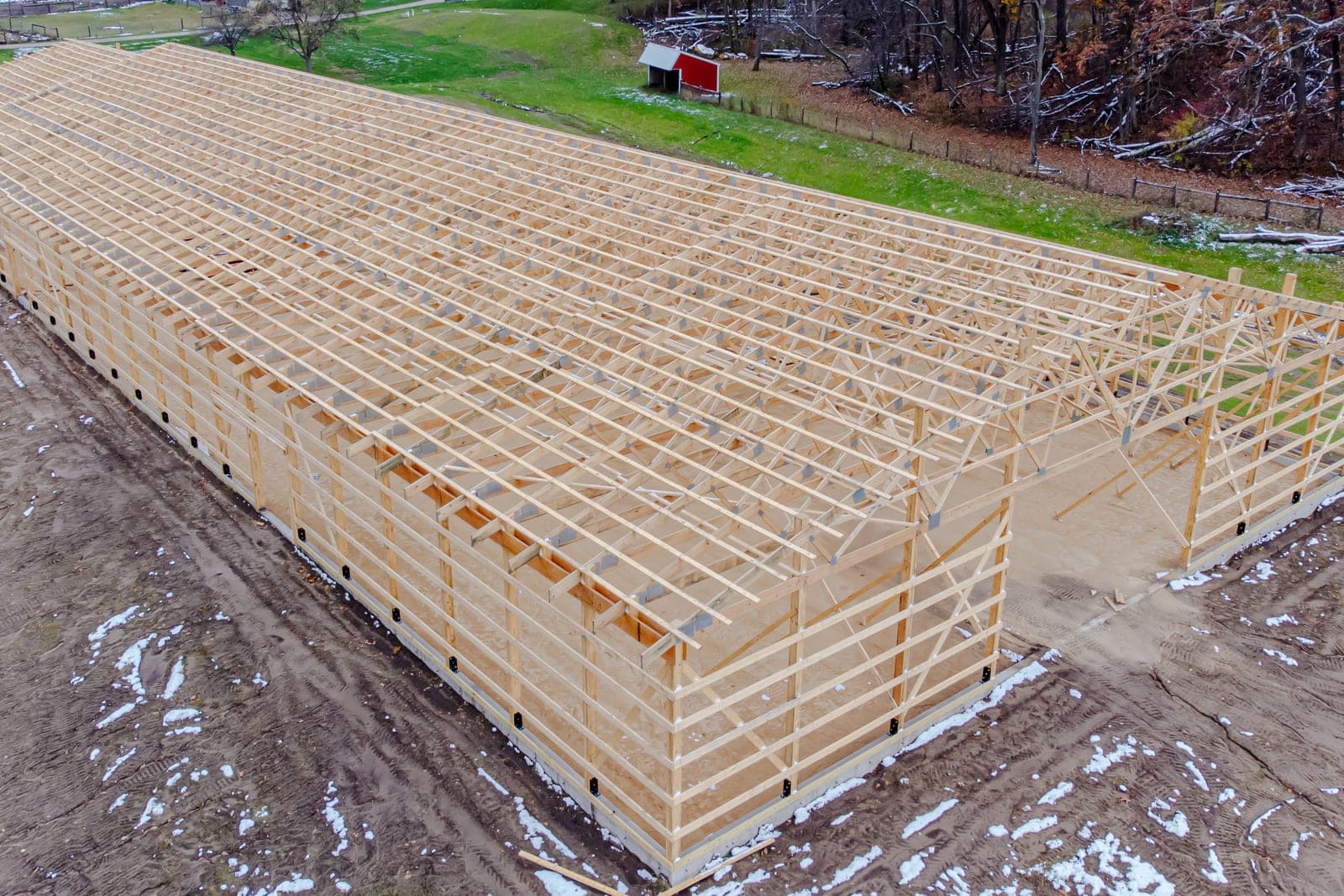 An aerial view of the long wood frame of a building under construction on a muddy site beside a green field
