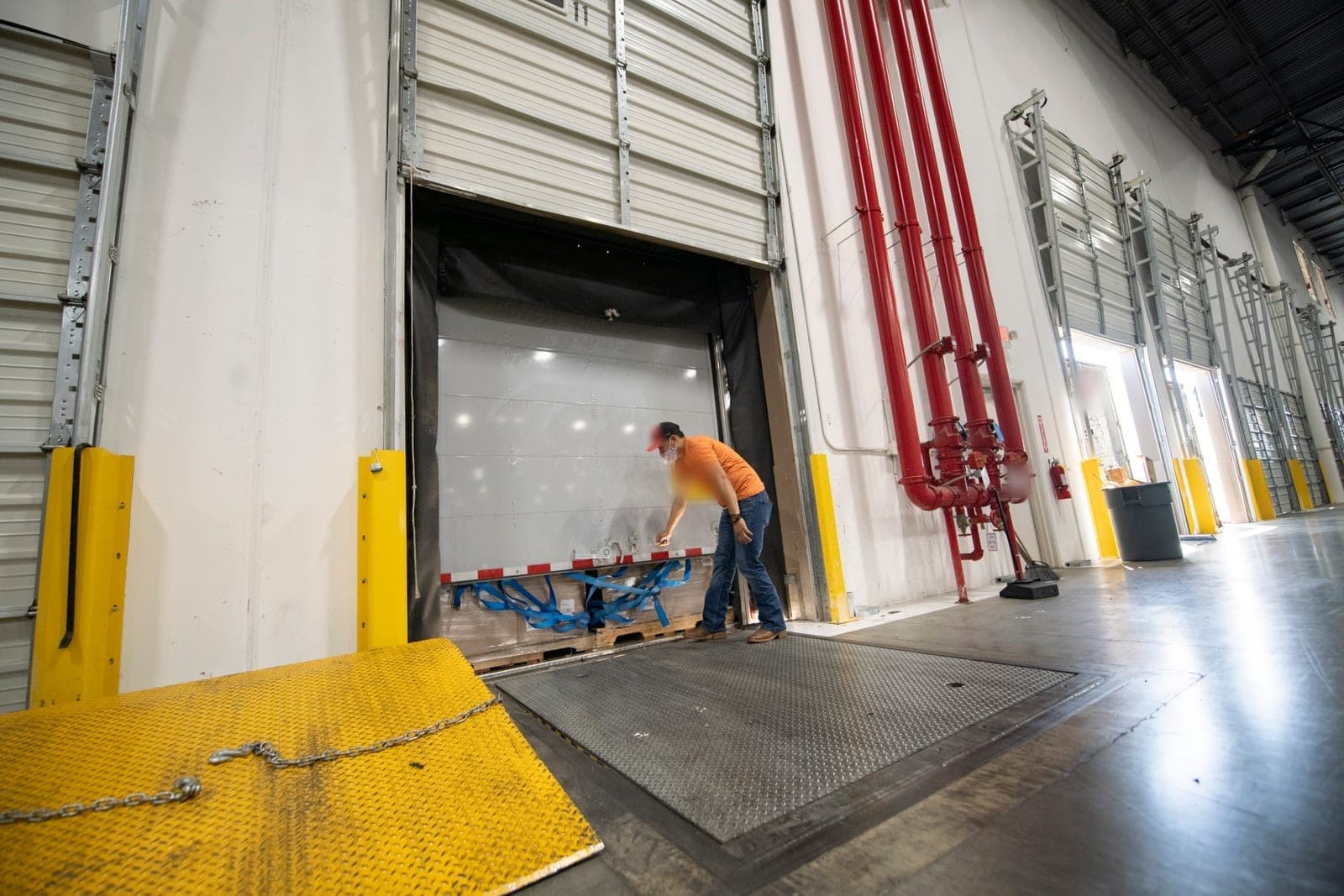 A trailer backed into a warehouse dock door while a worker opens its rear doors