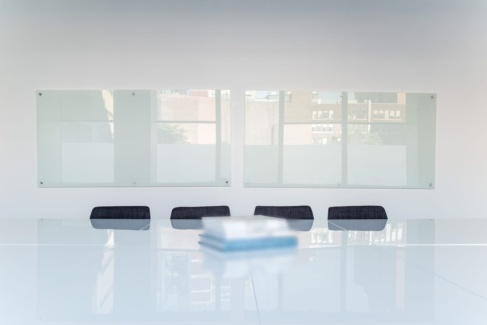 A quiet room with a white table, four chairs, two glass whiteboards and a stack of books