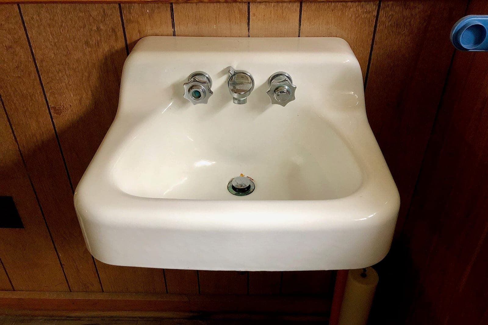 A white wall-mounted sink with chrome taps against wood paneling