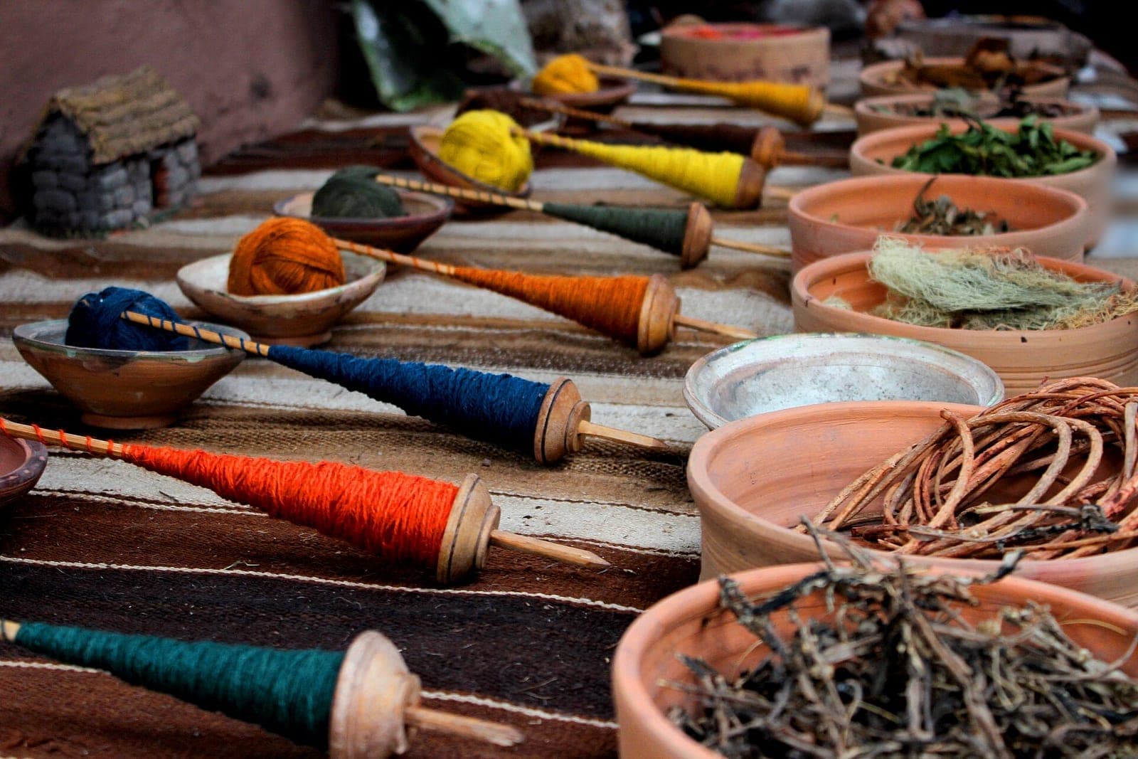 Spindles of dyed yarn and clay bowls of dried plants laid out on a striped market table