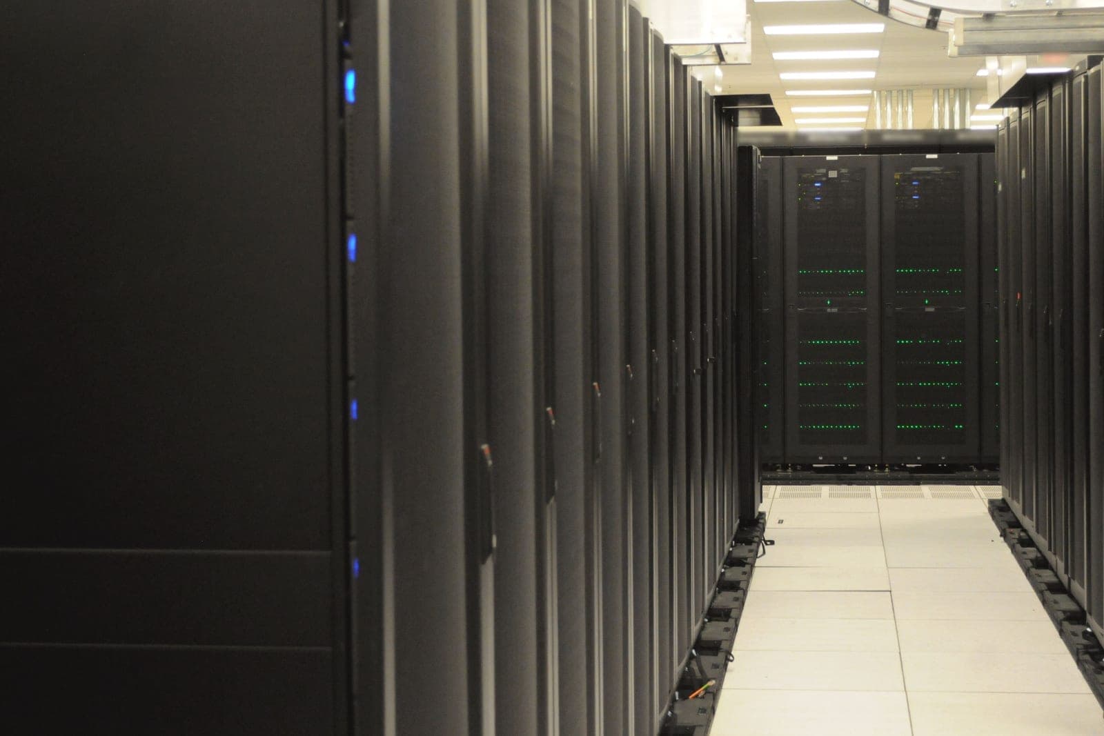 Rows of tall black server cabinets line both sides of a bright aisle with a white tiled floor