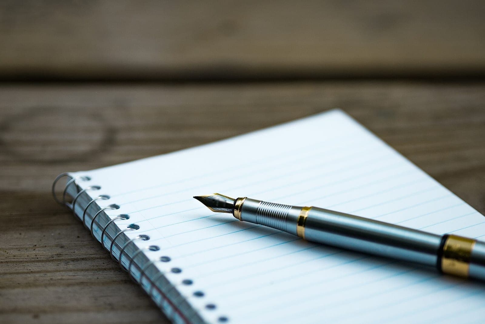 A silver fountain pen rests on a blank lined notepad on a wooden table