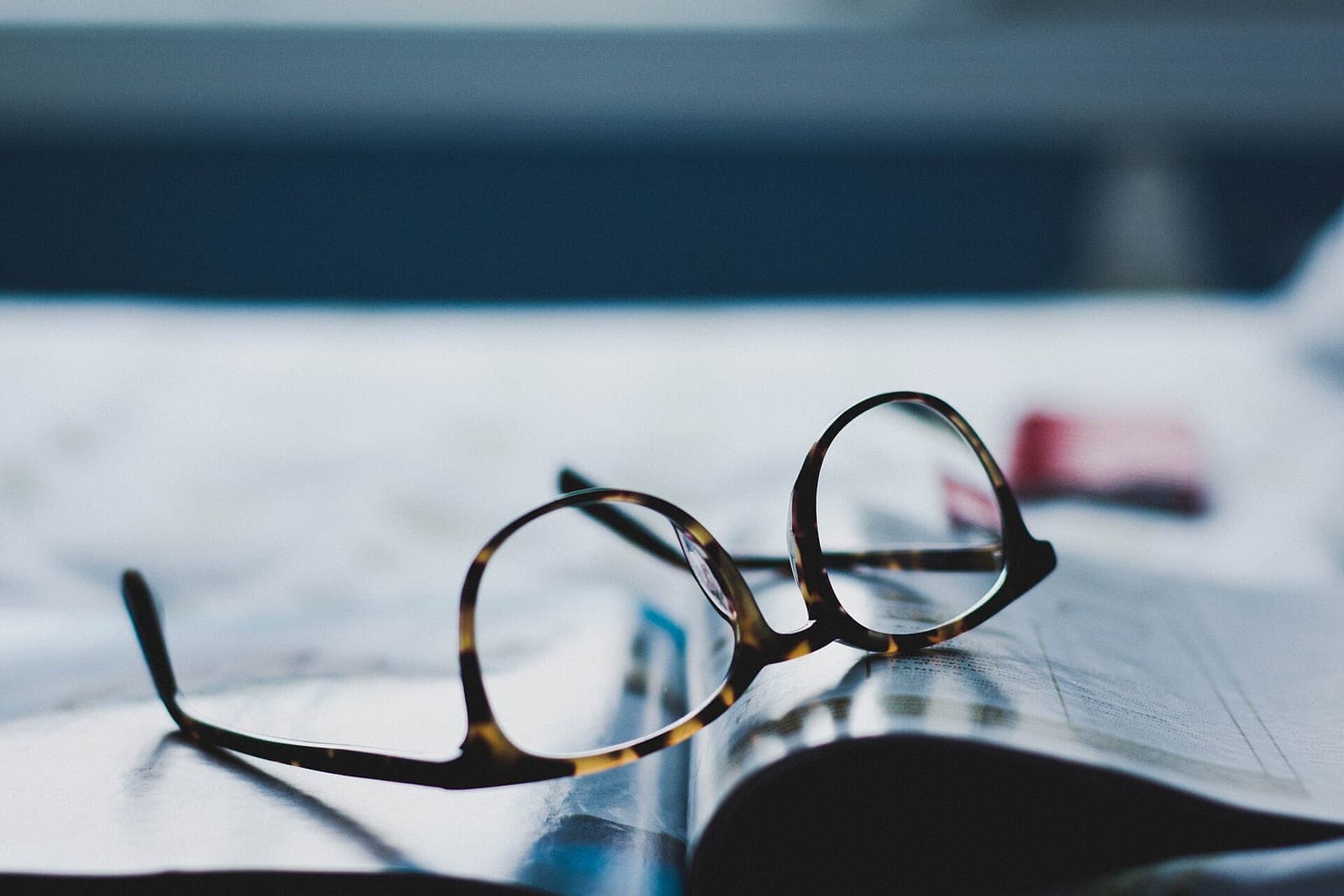 Tortoiseshell reading glasses rest on an open magazine on a table