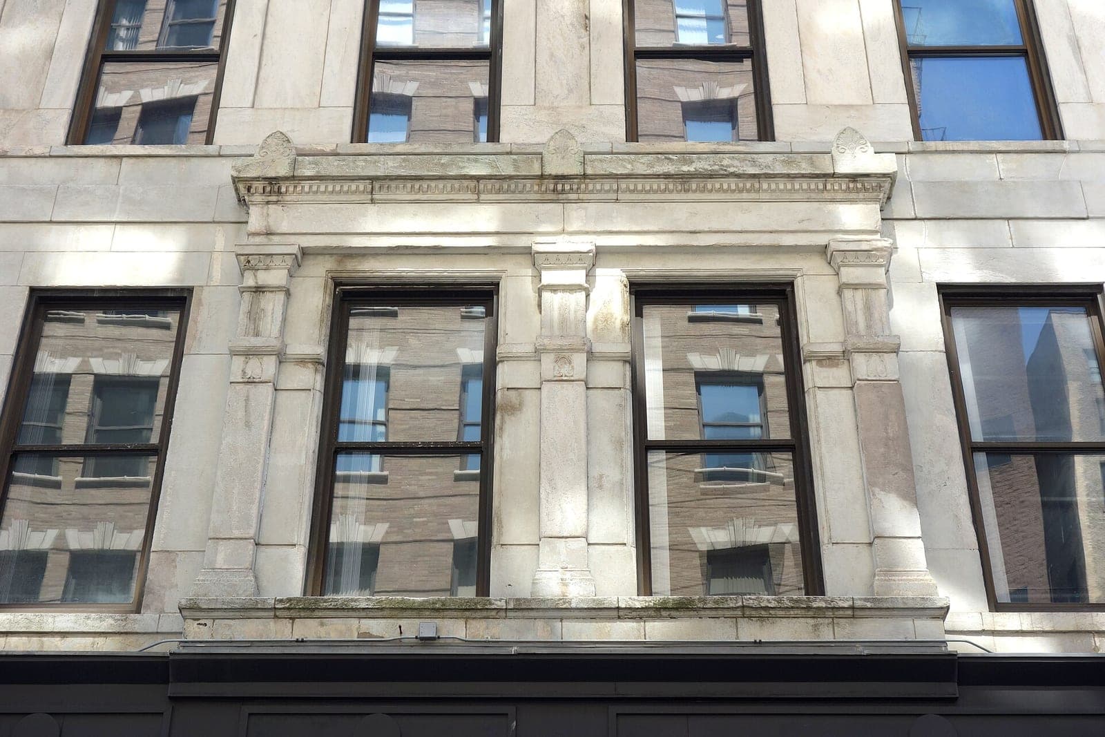 Tall windows in a pale stone office building, each pane reflecting the brick building across the street